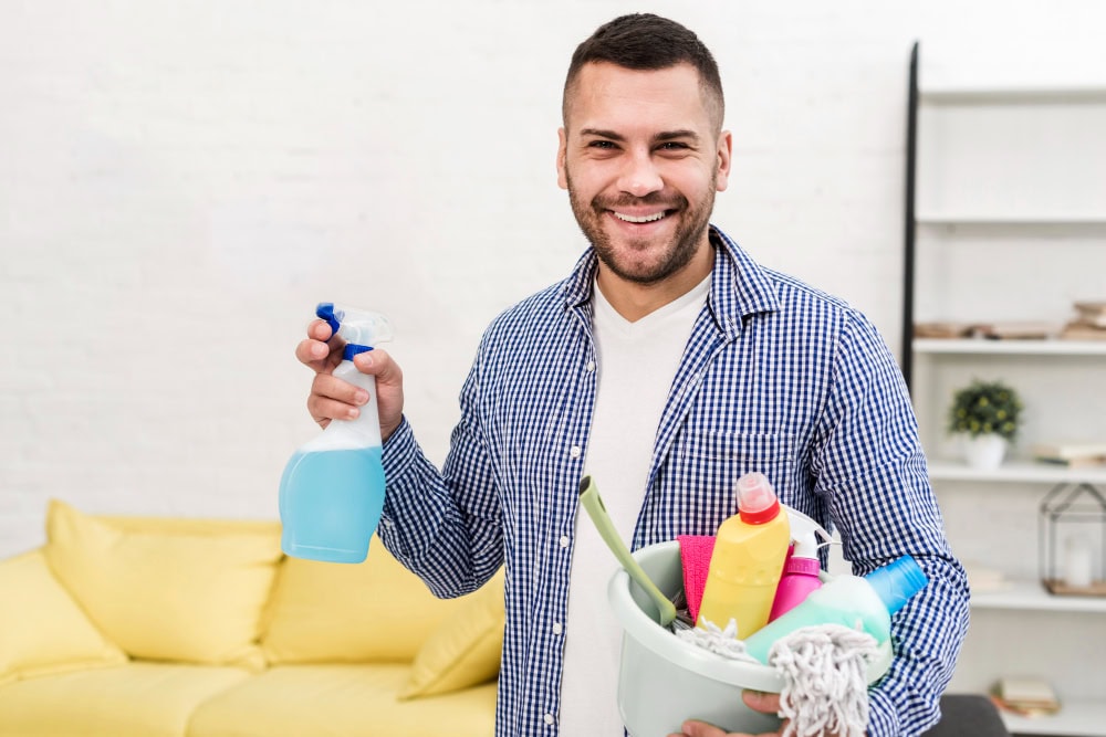 Hombre sosteniendo un kit de limpieza; las esponjas y paños visibles en el cubo son productos que habitualmente requieren envases tipo blister para su venta en retail.